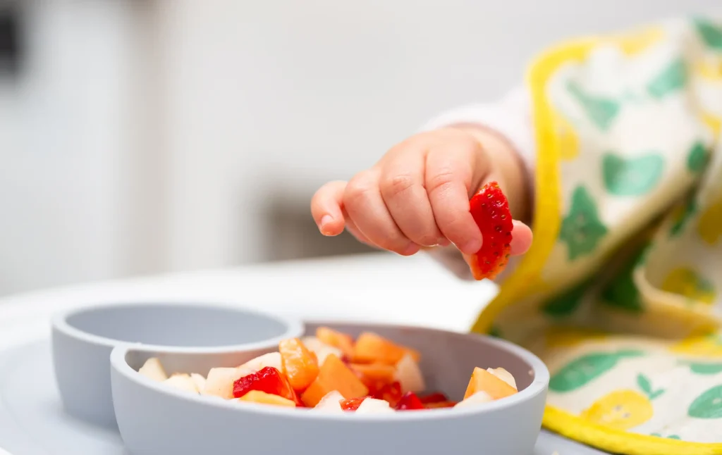 Une petite main qui saisi des fruits dans une petite assiette