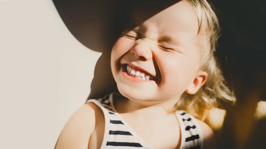 Petite fille blonde en débardeur rayé bleu marine qui ferme les yeux le visage illuminé par le soleil