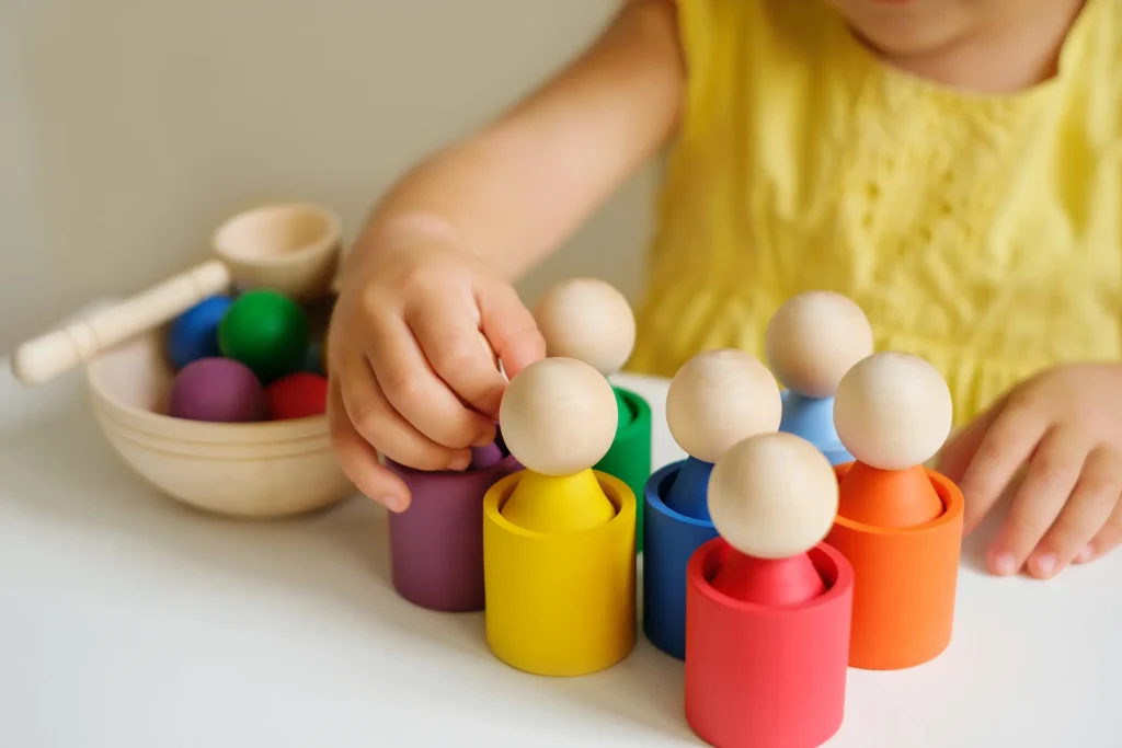 Petite fille portant une robe jaune qui joue avec des petits personnages en bois colorés