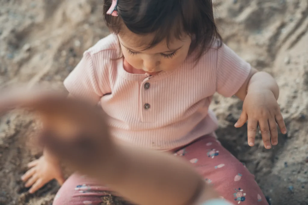 Enfant assis sur le sable, portant un haut rose à manches courtes et un pantalon rose avec des motifs
